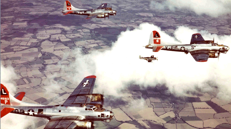 Aerial view of three Boeing B-17 Flying Fortress bombers, escorted by a North American P-51 Mustang fighter over England