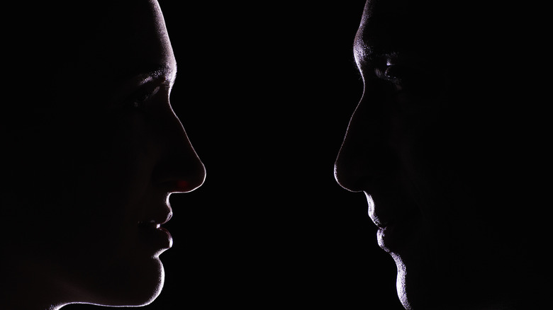 two backlit men staring at each other dark background