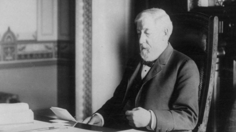 James G Blaine in suit reading at desk