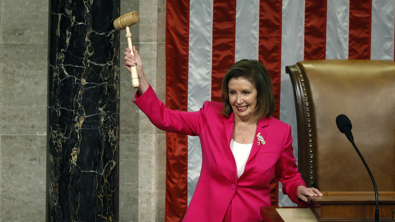 Nancy Pelosi raising gavel red suit by chair