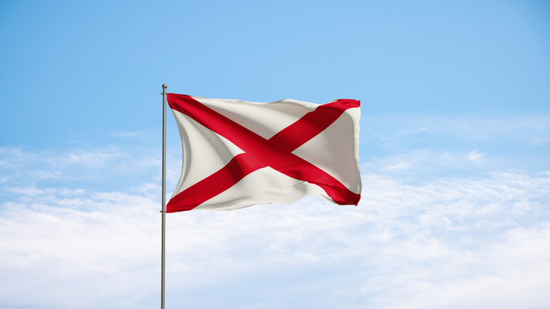 Alabama state flag against pale blue sky white white clouds