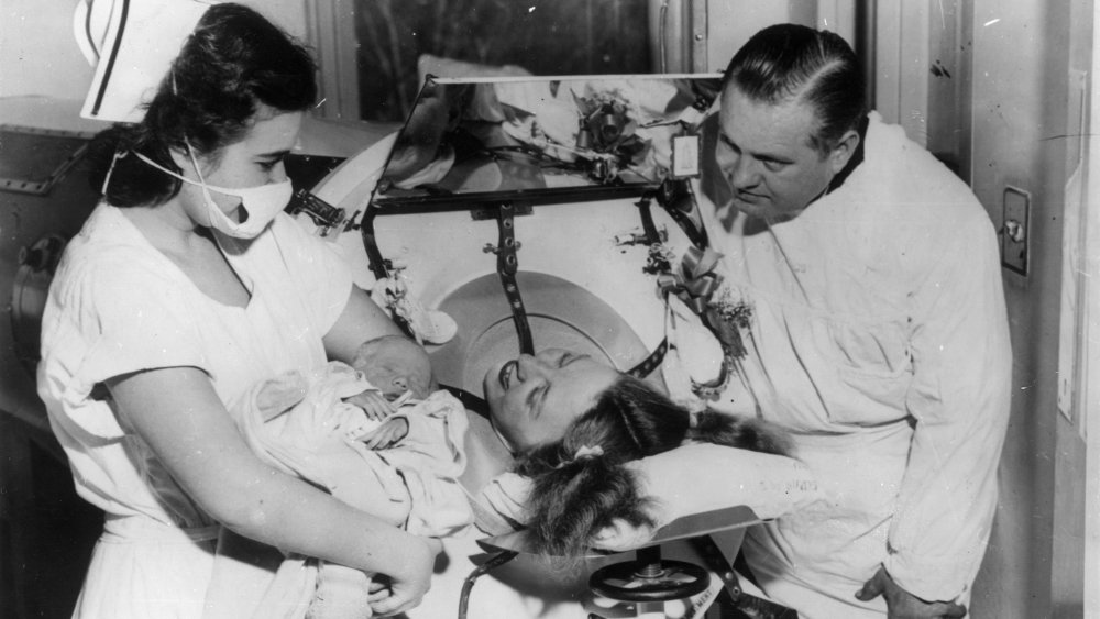 1953: A woman seeing her new born baby whilst lying inside an iron lung as part of her treatment for Polio.