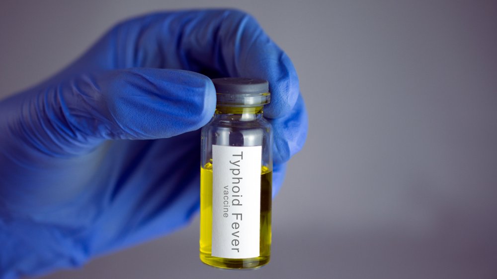 Hands in blue gloves holding a jar with a yellow vaccine.