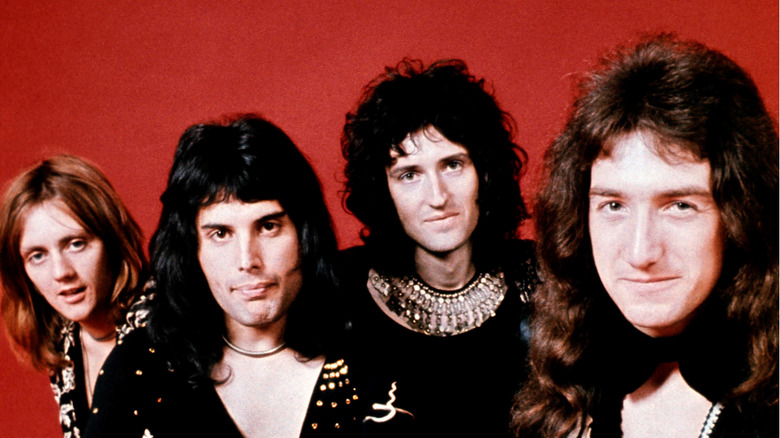 the band Queen posing in front of a red back drop