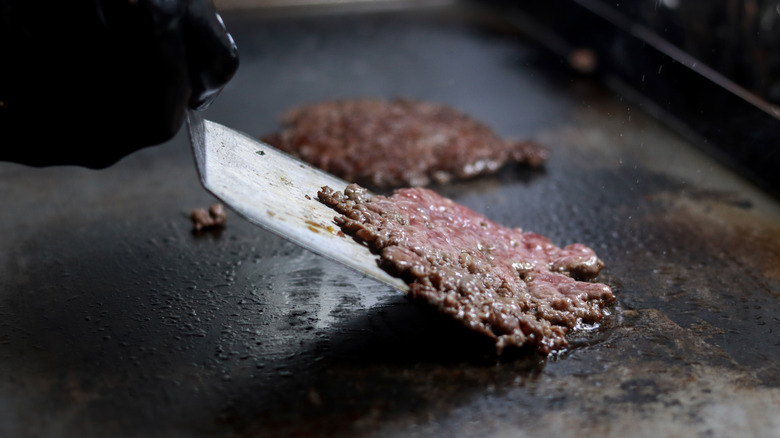 A gloved hand flipping a burger with a spatula