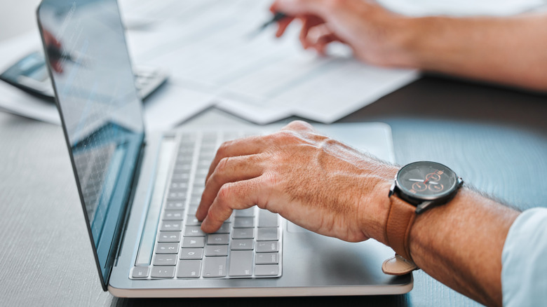 A man working on a laptop while writing on paper