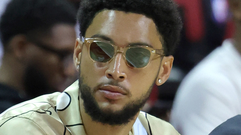 Ben Simmons sitting courtside wearing sunglasses