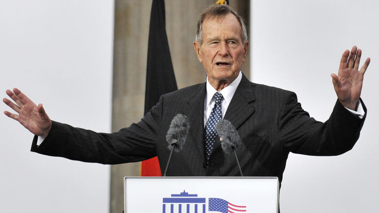 George Bush Senior standing in suit at lectern arms raised talking