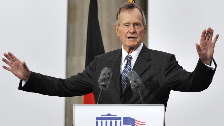 George Bush Senior standing in suit at lectern arms raised talking