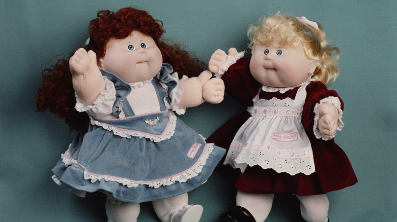 two cabbage patch kids dolls in front of a fabric backdrop