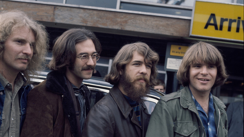John and Tom Fogerty with other members of Creedence Clearwater Revival smiling at Heathrow Airport