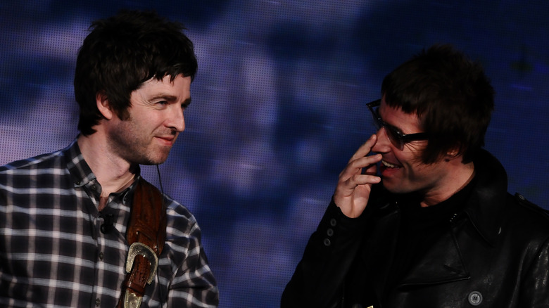 Liam and Noel Gallagher of Oasis smiling at each other on stage