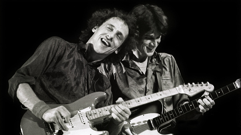 Mark and David Knopfler of Dire Straits leaning close together while playing guitars on stage