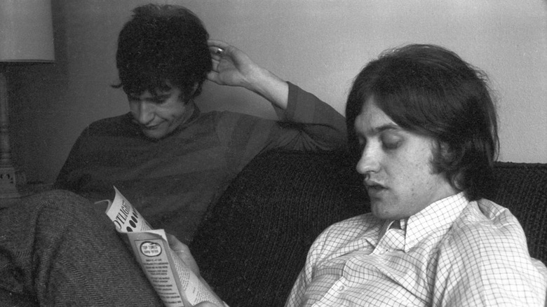 Ray and Dave Davies of The Kinks reading magazines on a couch in a hotel room