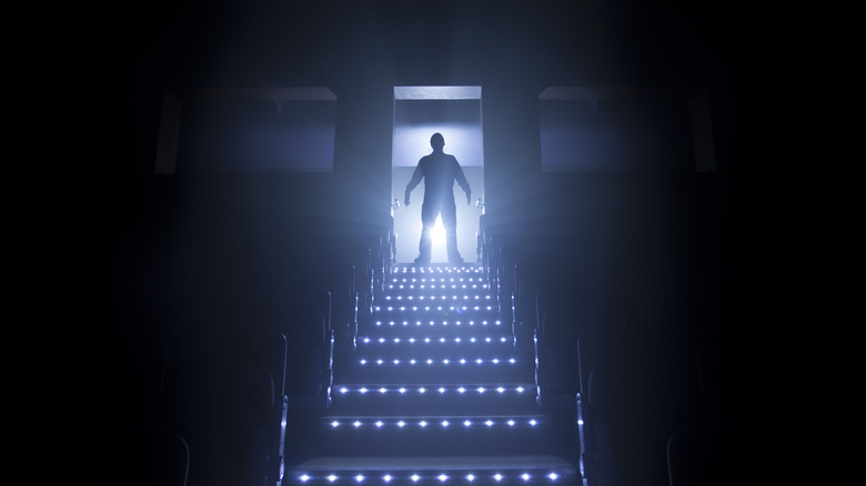 creepy figure silhouetted at top of illuminated theater stairs