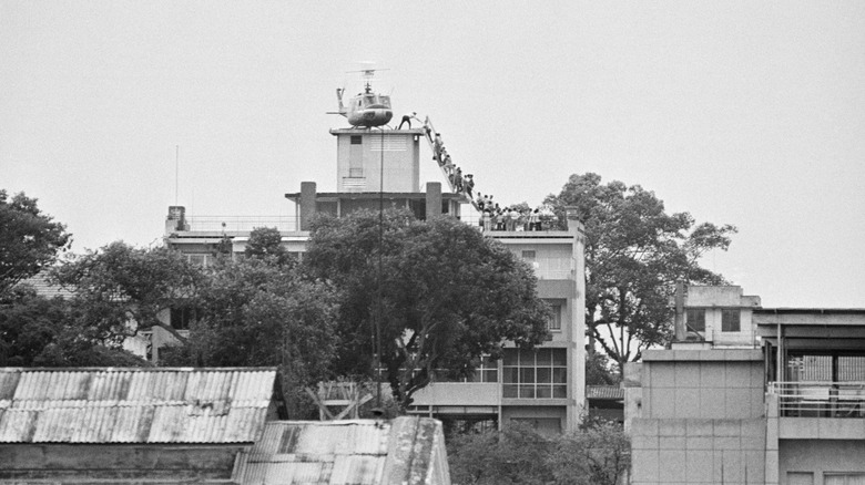 A CIA employee helps people fleeing Saigon onto a helicopter