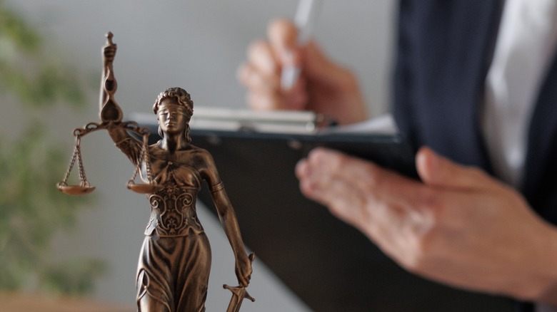 A lawyer makes notes behind a statue of justice