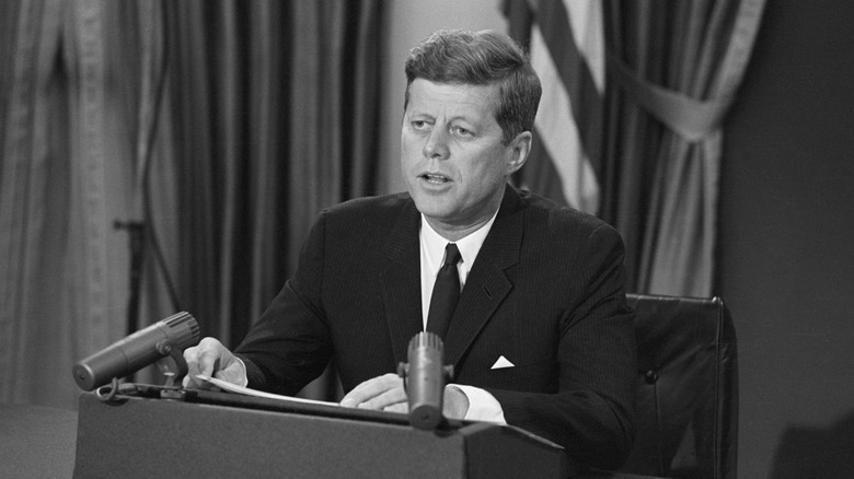 JFK seated behind desk with microphones