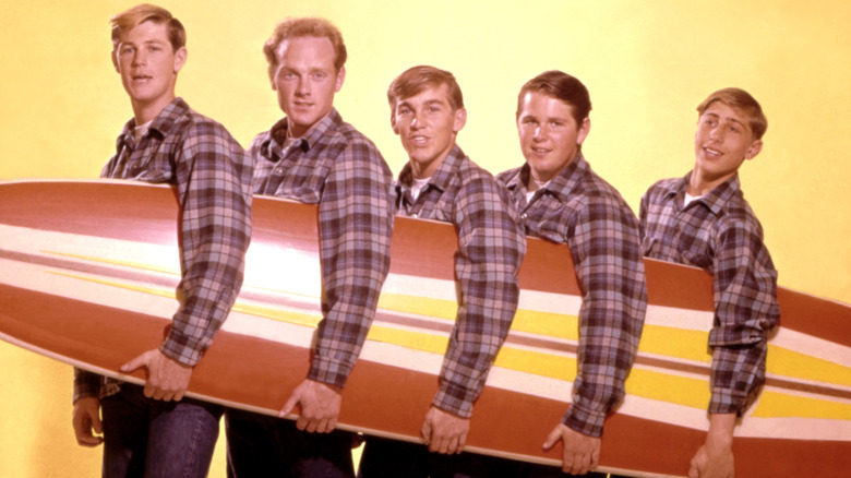 The Beach Boys pose for a portrait with a surfboard in august 1962. (L-R) Brian Wilson, Mike Love, Dennis Wilson, Carl Wilson, David Marks