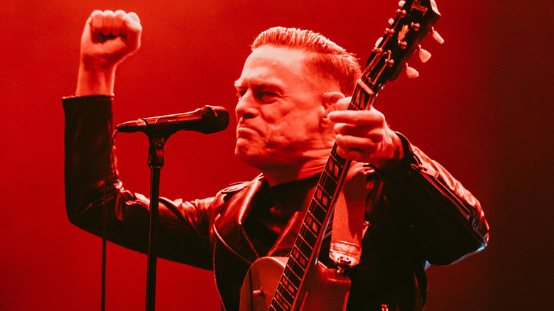 Bryan Adams holding guitar and pumping fist onstage