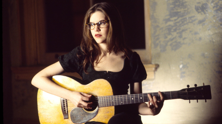 Lisa Loeb playing acoustic guitar and staring to side