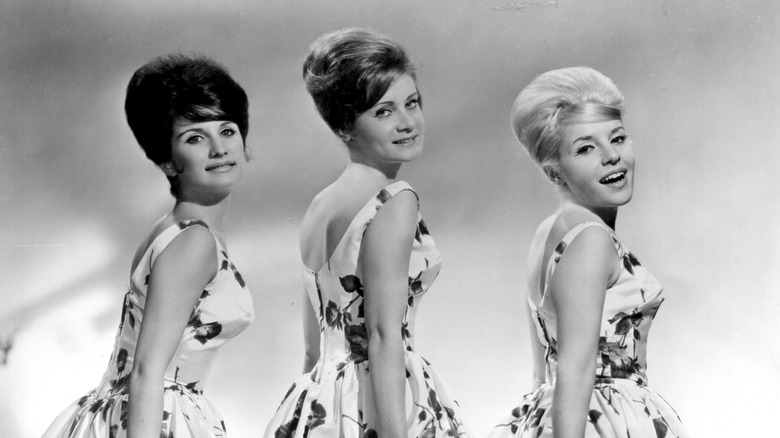 Black and white photo of Peggy Santiglia, Barbara Allbut, and her sister Phyllis in floral sleeveless dresses looking over their shoulders