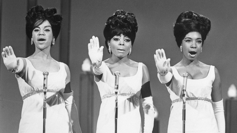 The Supremes singing on stage, with arms outstretched.