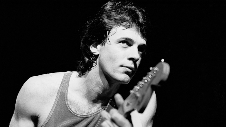 Rick Springfield playing guitar on stage with black background