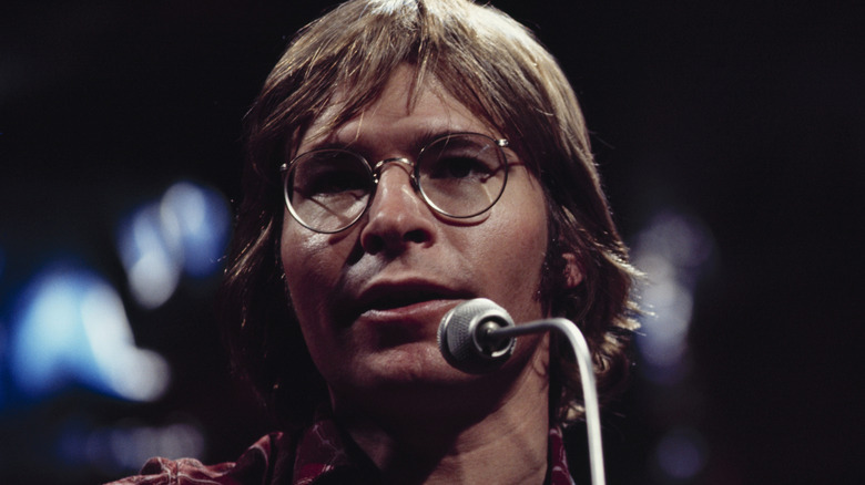 John Denver at a mic onstage in the 1970s