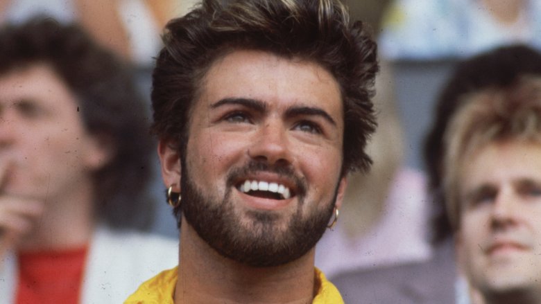 George Michael with earrings and beard smiling in crowd