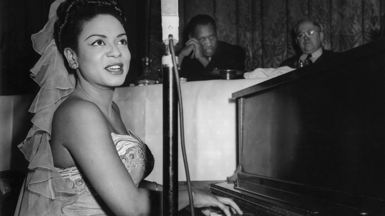 Hazel Scott in dress smiling and playing piano