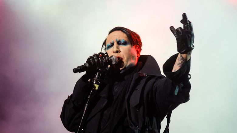 marilyn manson black jacket and gloves singing on stage arm raised