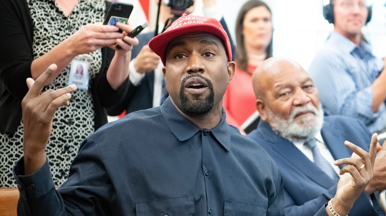 Kanye West in shirt arms raised wearing MAGA hat at event