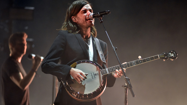 Winston Marshall playing a banjo and singing on stage for Mumford & Sons