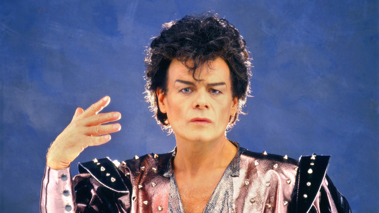 Gary Glitter in costume hand raised blue background