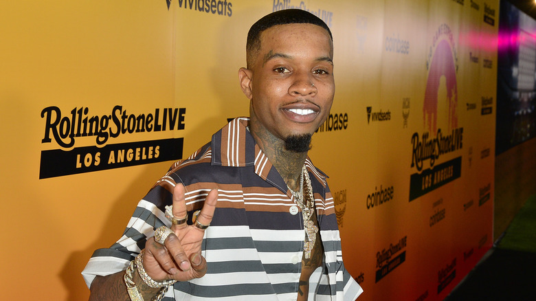 Tory Lanez smiling showing a peace sign in striped shirt and jewelry at event