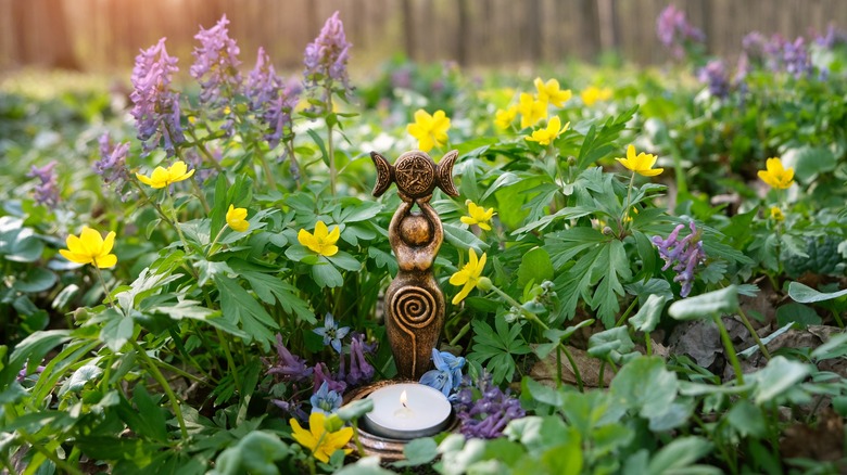 Triple goddess candlestick amongst flowers