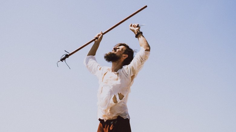 Man in rags shaking stick