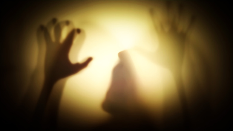 Ghostly raised arms backlit with shadowy cloaked figure in background