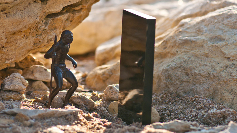 Black monolith on old sandstone rock near the sea coast and Cro-Magnon man with a spear