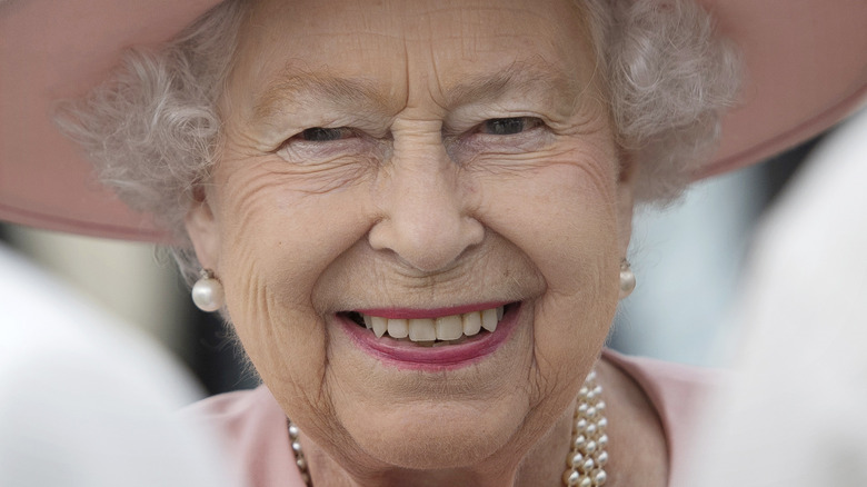 Queen Elizabeth II smiles in a pink hat