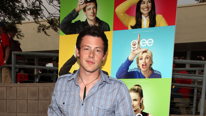 Corey Monteith posing in front of a Glee poster