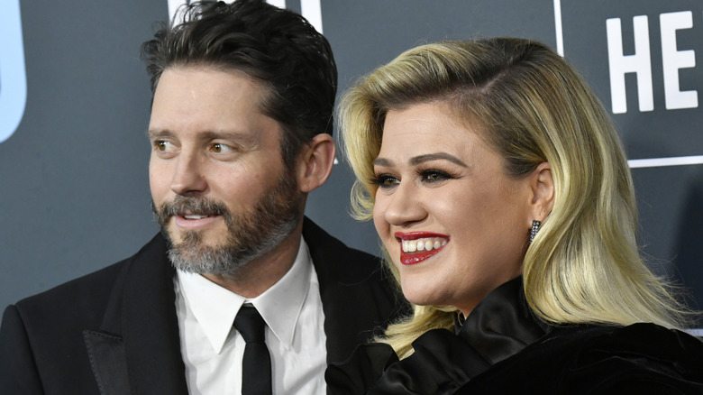 Brandon Blackstock in suit with Kelly Clarkson in black dress smiling at event