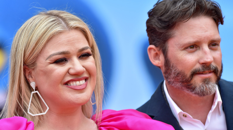 Kelly Clarkson smiling in pink dress with Brandon Blackstock in suit at event