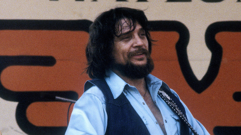 Waylon Jennings smiling while playing guitar on stage