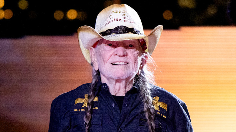 Willie Nelson wearing hat and half smiling on stage
