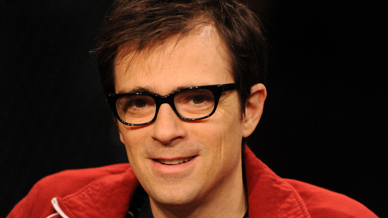 Rivers Cuomo smiling wanly in red jacket