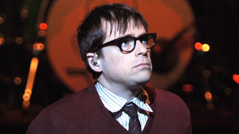 Rivers Cuomo on stage in 90s in sweater looking up and off