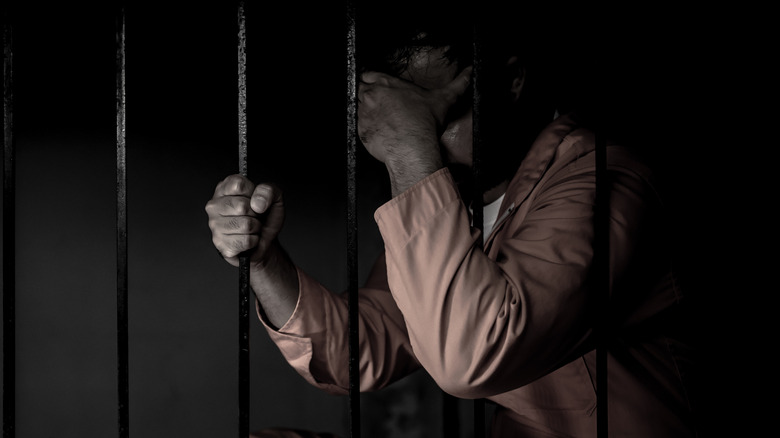 Man hiding his face behind prison bars