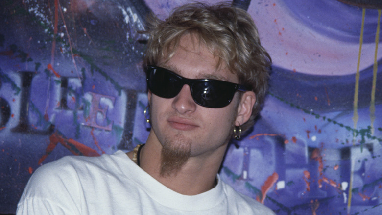 Layne Staley sitting by a mural in sunglasses looking away